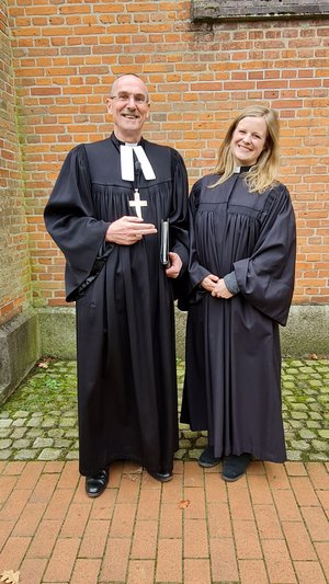 Ein Mann und eine Frau in geistlicher Kleidung lächeln in die Kamera
