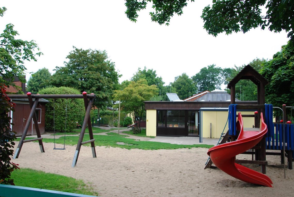 Klettergerüst mit geschwungener roter Rutsche, links eine Schaukel