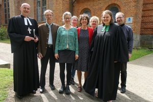 Acht Menschen im Sonnenschein vor einer Kirche