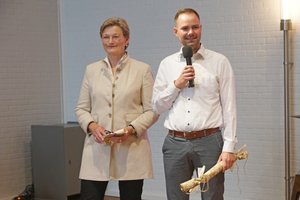 Ein Mann spricht in ein Mikro, daneben steht eine Frau
